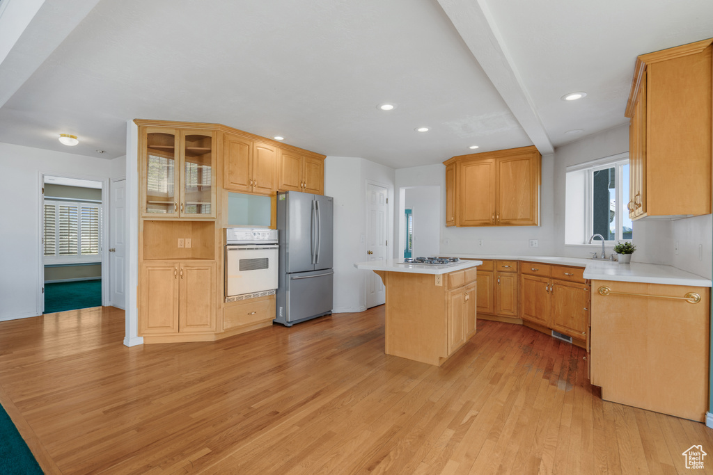 Kitchen with appliances with stainless steel finishes, a center island, a breakfast bar, beam ceiling, and light hardwood / wood-style flooring