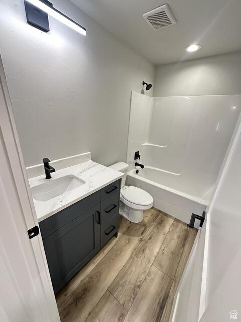 Full bathroom with tub / shower combination, toilet, vanity, and hardwood / wood-style floors