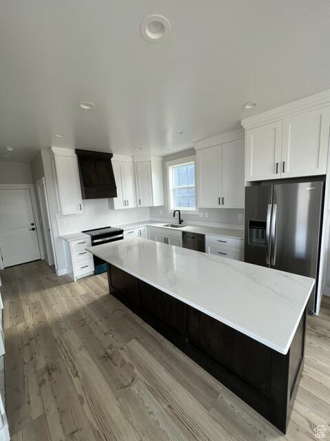 Kitchen featuring range hood, black dishwasher, a center island, and light wood-type flooring