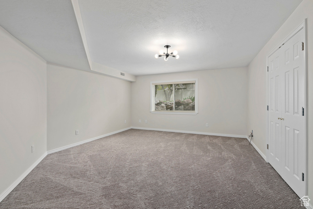 Carpeted empty room featuring an inviting chandelier