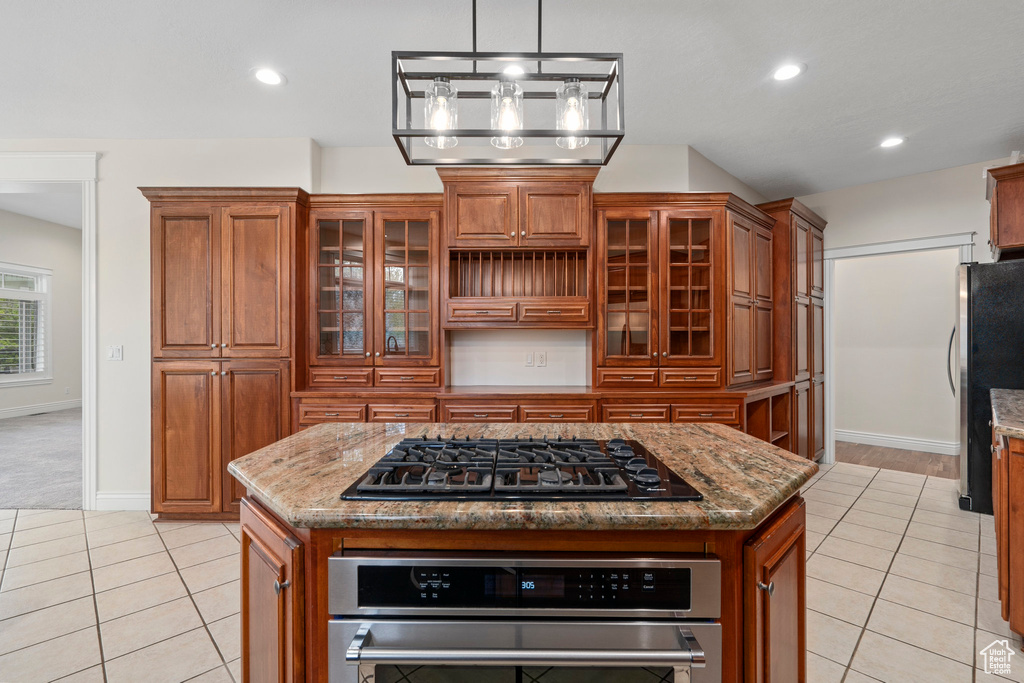 Kitchen with appliances with stainless steel finishes, a kitchen island, dark stone countertops, pendant lighting, and light tile floors