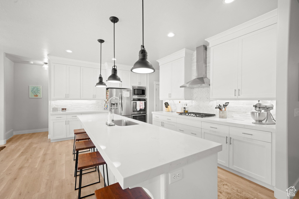 Kitchen with appliances with stainless steel finishes, wall chimney range hood, tasteful backsplash, and a kitchen island with sink