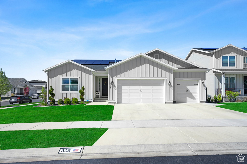 View of front of property featuring solar panels, a garage, and a front lawn