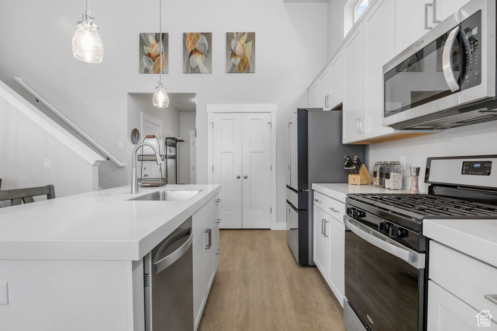 Kitchen featuring white cabinets, light hardwood / wood-style flooring, stainless steel appliances, sink, and an island with sink