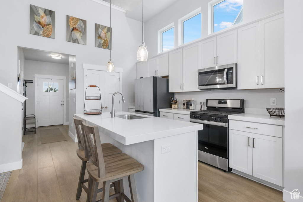 Kitchen featuring appliances with stainless steel finishes, hanging light fixtures, white cabinets, and light hardwood / wood-style flooring