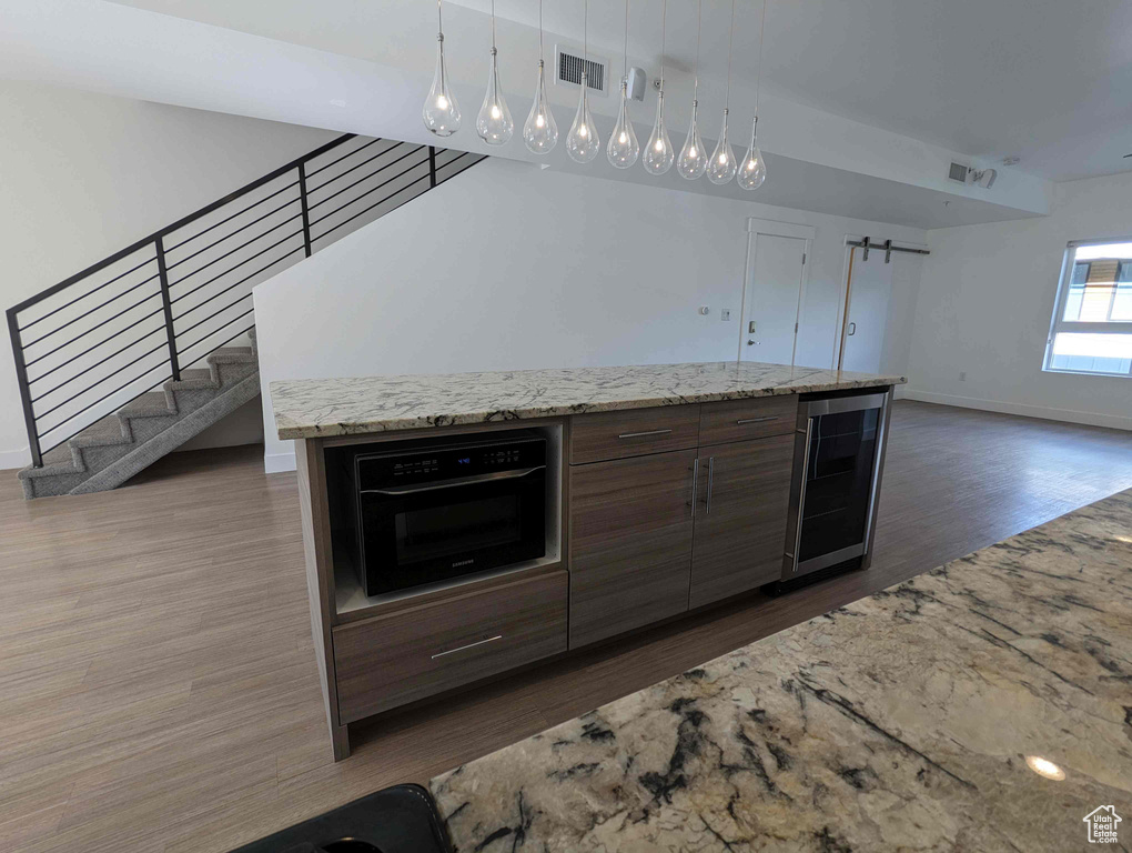 Kitchen with a center island, wine cooler, decorative light fixtures, wood-type flooring, and black oven