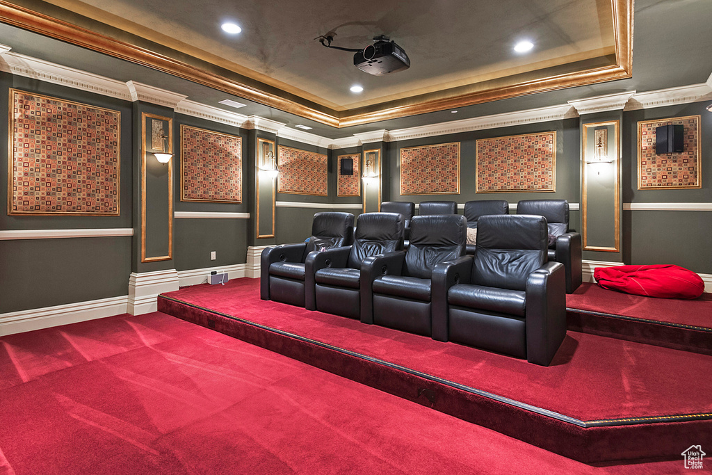 Carpeted home theater room with a tray ceiling and ornamental molding