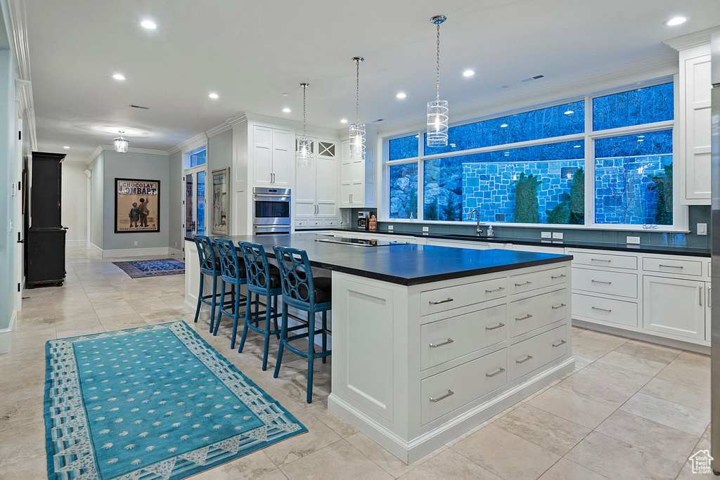 Kitchen featuring a center island, pendant lighting, white cabinetry, ornamental molding, and backsplash