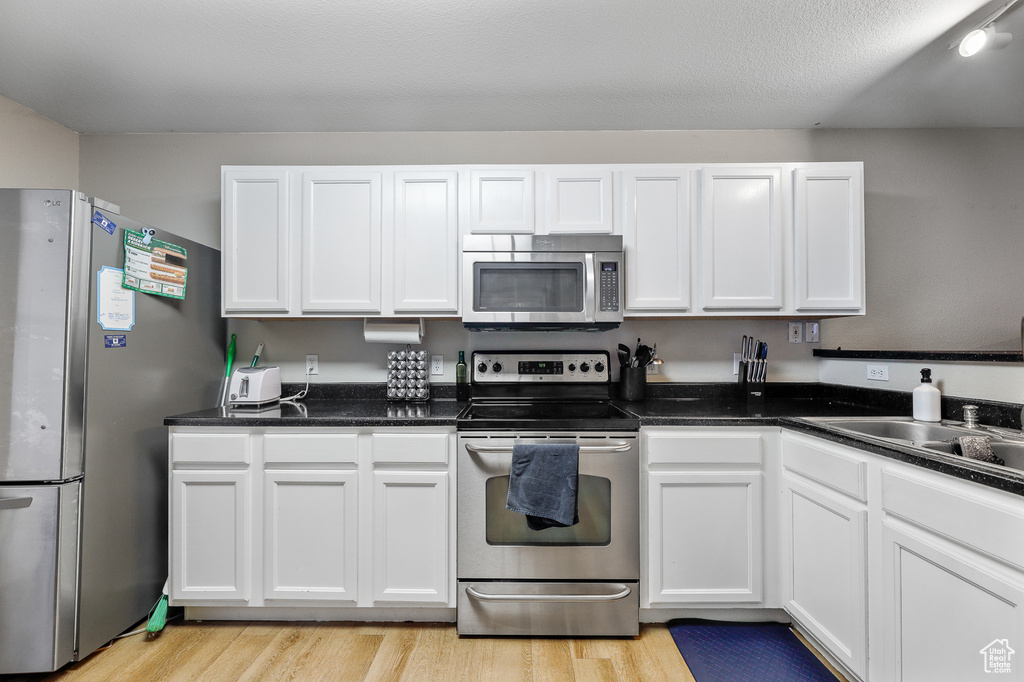 Kitchen with appliances with stainless steel finishes, light hardwood / wood-style flooring, sink, and white cabinets