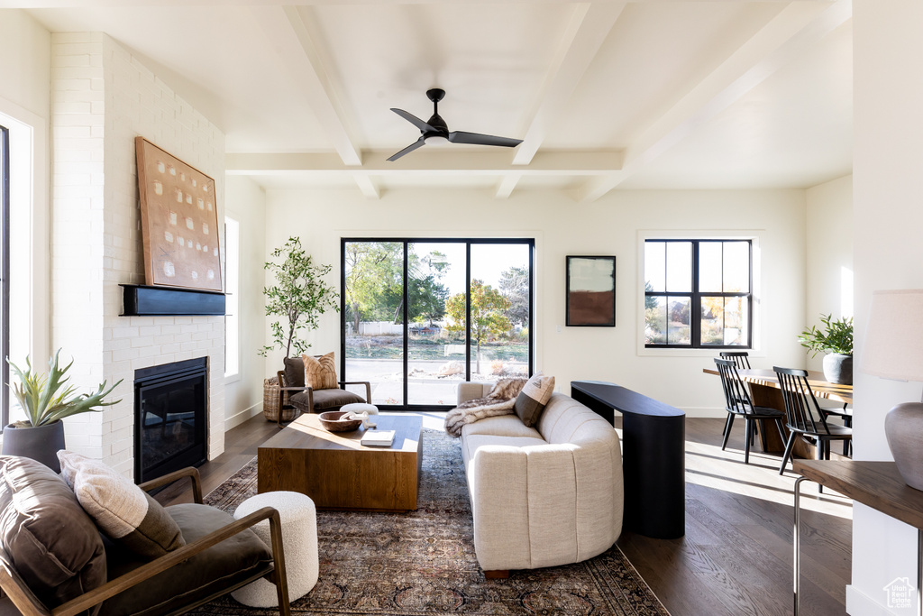 Living room featuring ceiling fan, a fireplace, brick wall, beam ceiling, and dark hardwood / wood-style floors