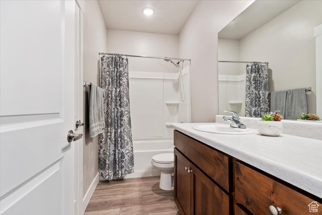 Full bathroom with hardwood / wood-style flooring, shower / tub combo, toilet, and vanity with extensive cabinet space