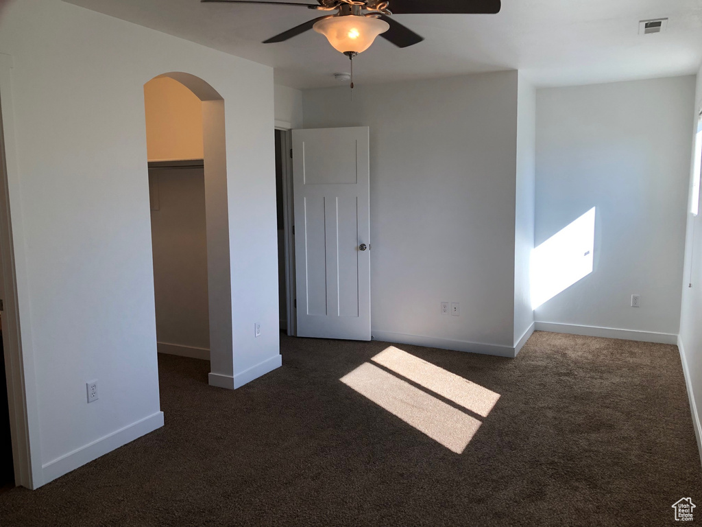 Unfurnished bedroom featuring a spacious closet, ceiling fan, dark carpet, and a closet