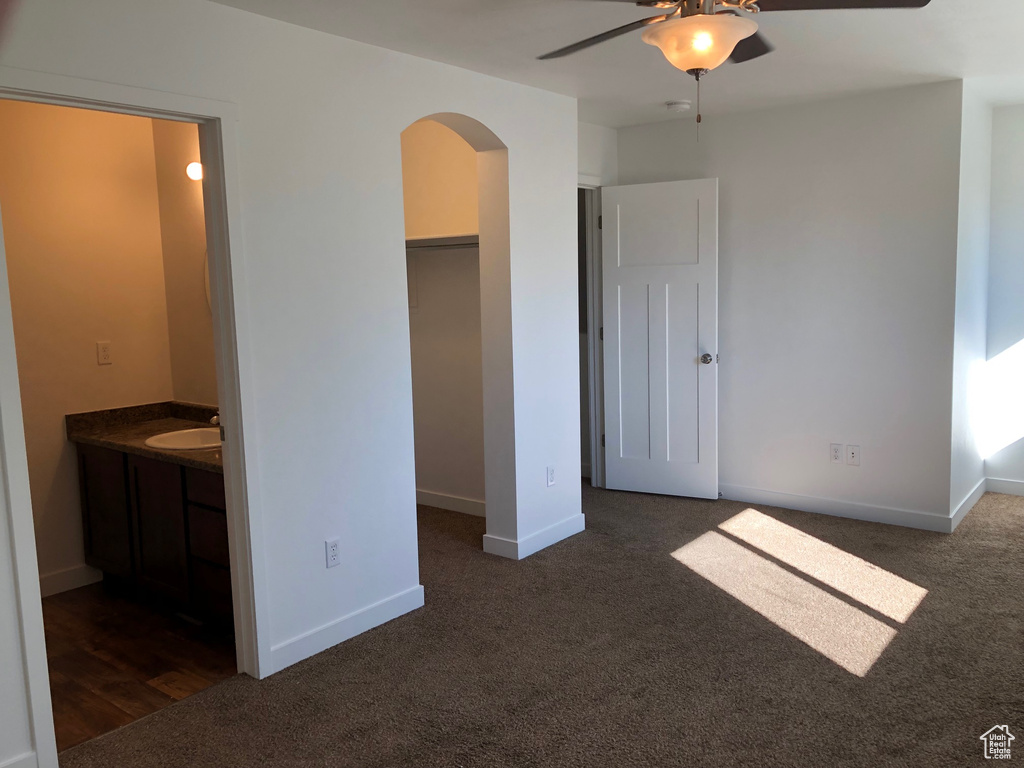 Unfurnished bedroom featuring a closet, sink, ensuite bath, a walk in closet, and dark carpet