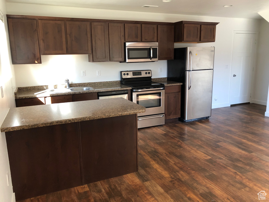 Kitchen with a kitchen island, appliances with stainless steel finishes, dark hardwood / wood-style flooring, and dark brown cabinets