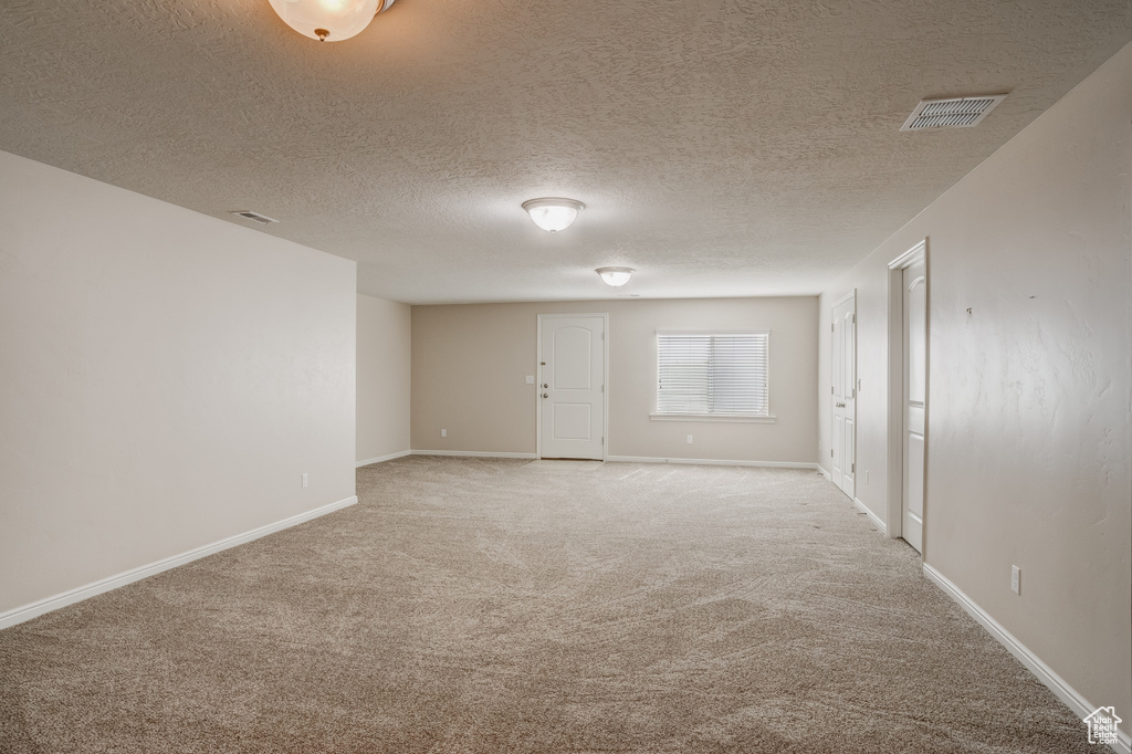 Unfurnished room featuring a textured ceiling and light carpet