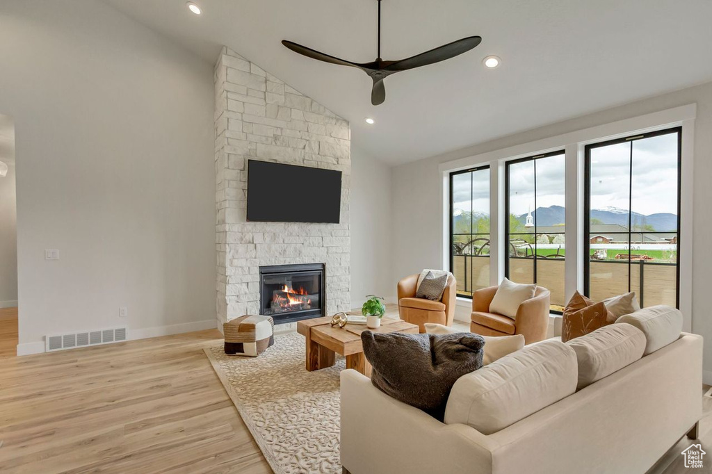 Living room featuring light hardwood / wood-style flooring, high vaulted ceiling, ceiling fan, and a stone fireplace