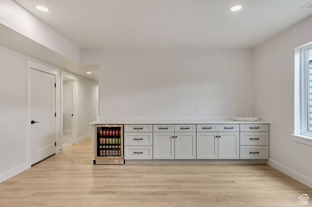 Interior space with wine cooler, light hardwood / wood-style flooring, and white cabinetry