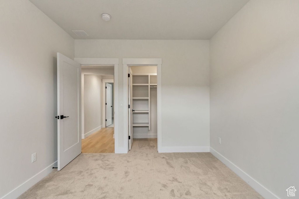 Unfurnished bedroom with light colored carpet, a spacious closet, and a closet