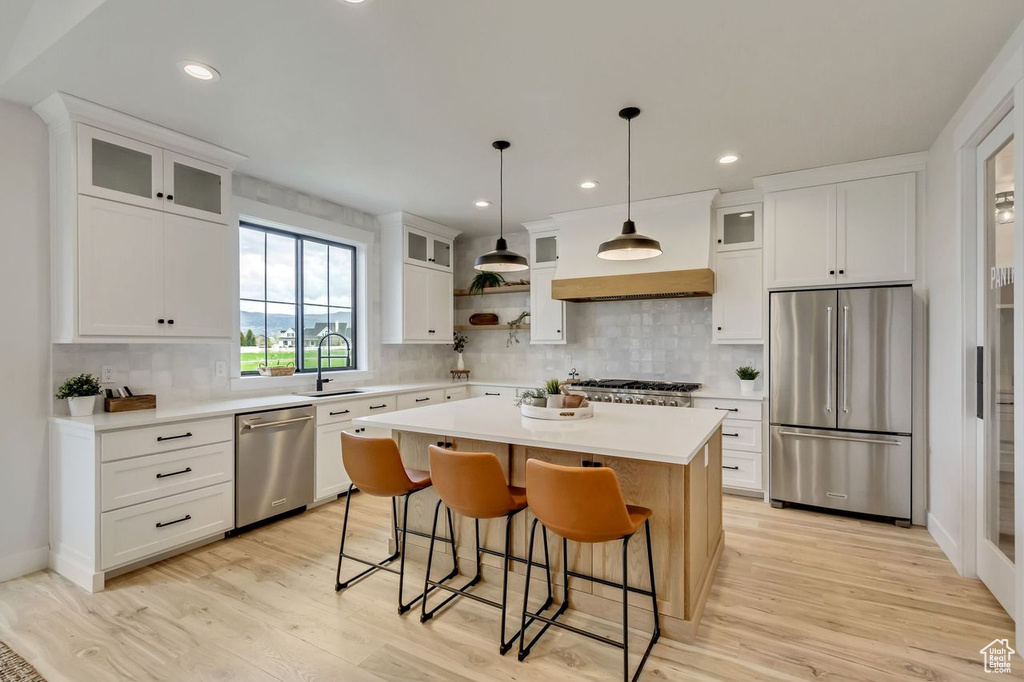 Kitchen featuring a kitchen island, appliances with stainless steel finishes, backsplash, and light wood-type flooring