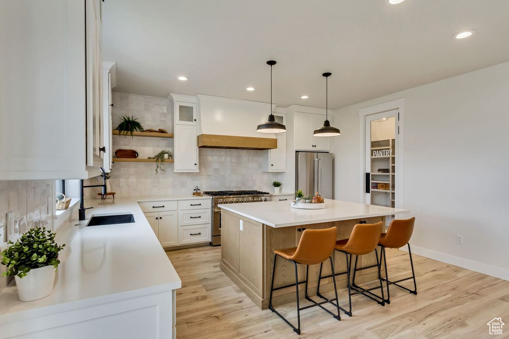 Kitchen with light hardwood / wood-style floors, tasteful backsplash, premium appliances, pendant lighting, and a center island