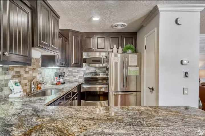 Kitchen with light stone countertops, sink, appliances with stainless steel finishes, backsplash, and dark brown cabinetry