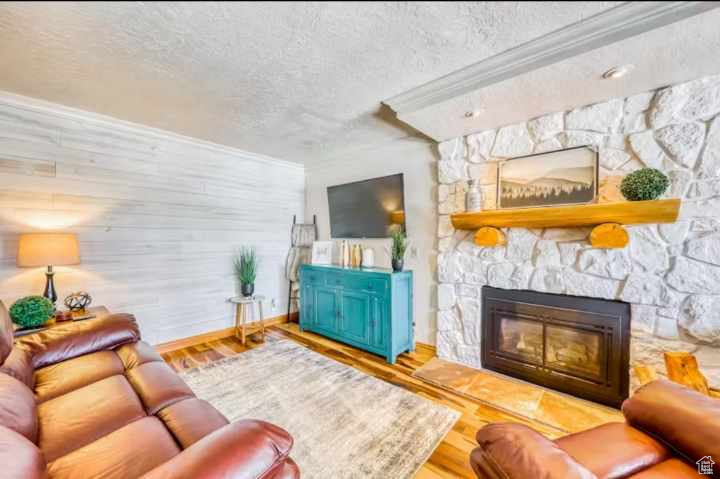 Living room featuring crown molding, hardwood / wood-style floors, a textured ceiling, and a fireplace