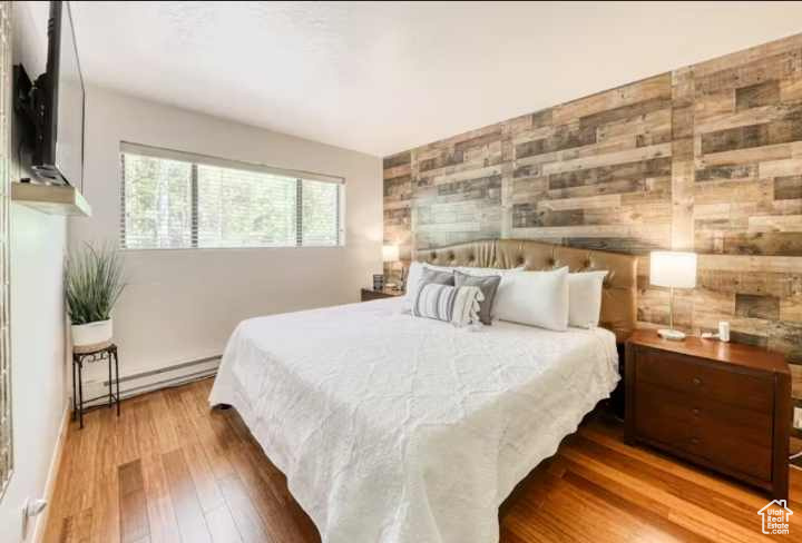 Bedroom with wood walls, hardwood / wood-style floors, and baseboard heating