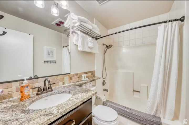 Full bathroom with backsplash, vanity, shower / bathtub combination with curtain, and toilet