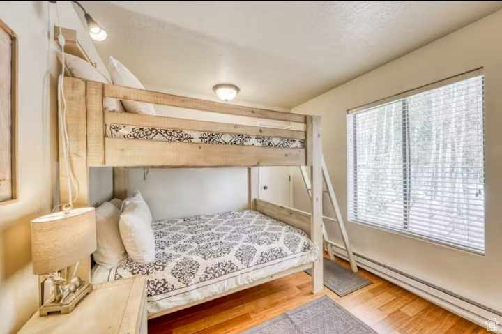 Bedroom with wood-type flooring, multiple windows, and baseboard heating