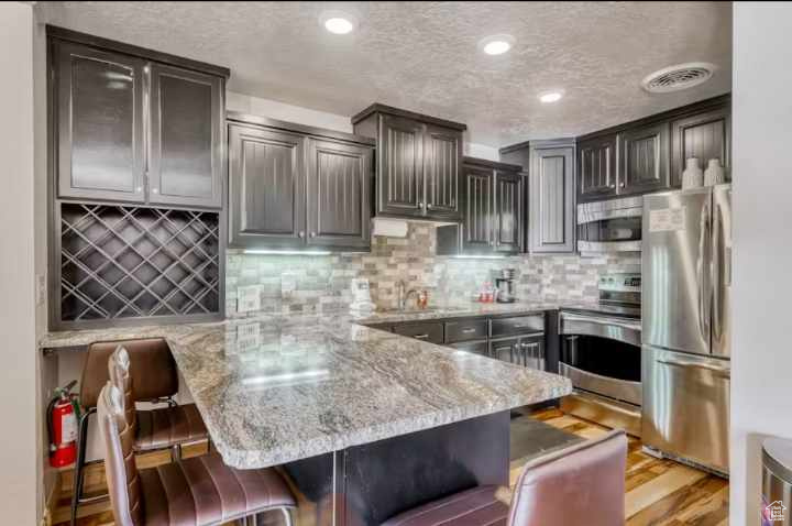 Kitchen featuring kitchen peninsula, appliances with stainless steel finishes, backsplash, a breakfast bar area, and light hardwood / wood-style floors