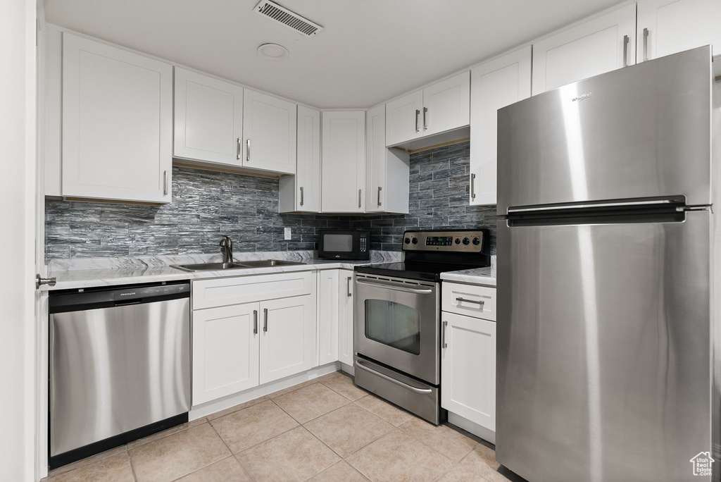 Kitchen with tasteful backsplash, stainless steel appliances, white cabinets, and light tile floors