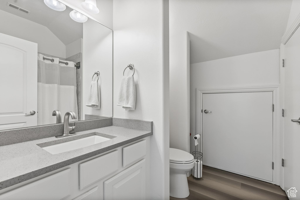 Bathroom with hardwood / wood-style floors, oversized vanity, vaulted ceiling, and toilet