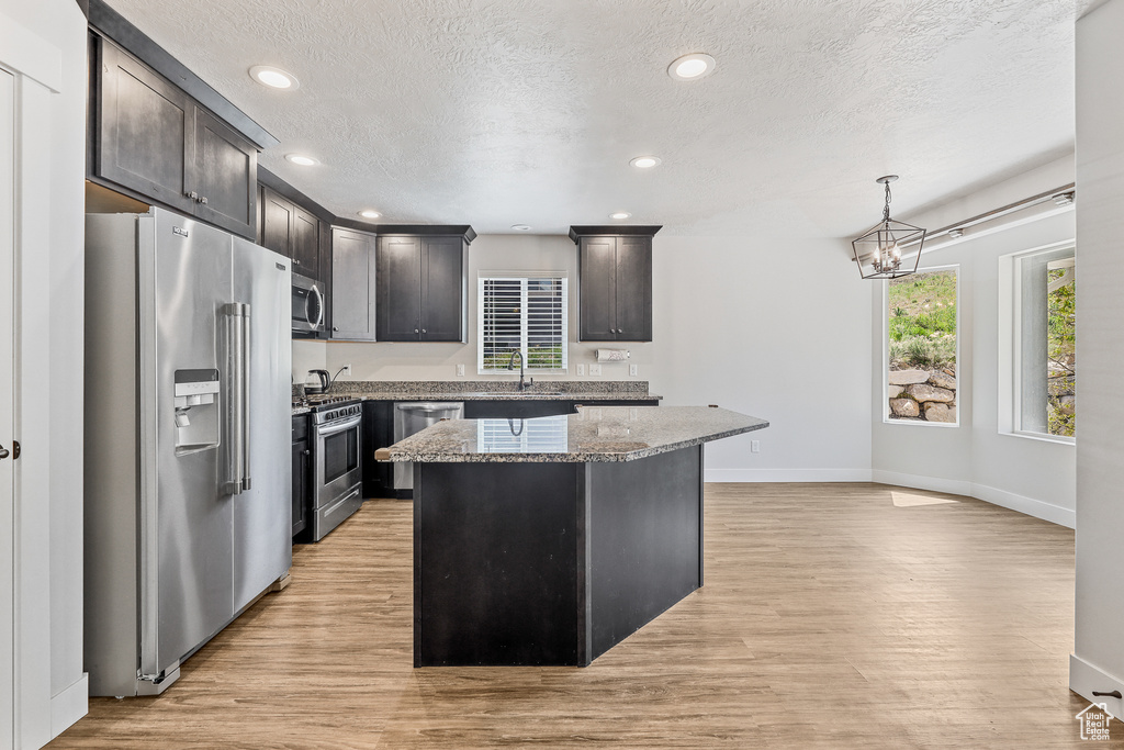 Kitchen featuring a kitchen island, pendant lighting, appliances with stainless steel finishes, and light wood-type flooring