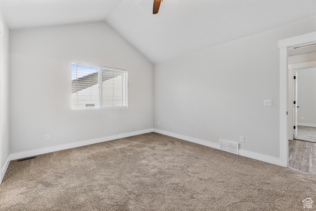 Empty room featuring carpet flooring, ceiling fan, and vaulted ceiling