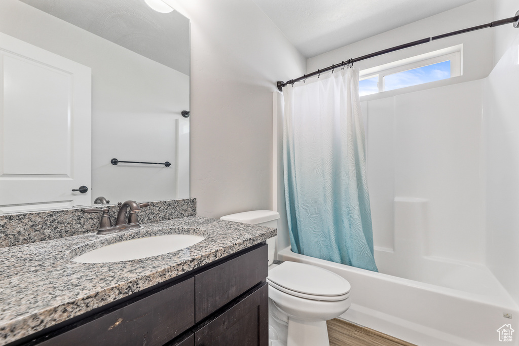 Full bathroom with wood-type flooring, vanity with extensive cabinet space, shower / bathtub combination with curtain, and toilet