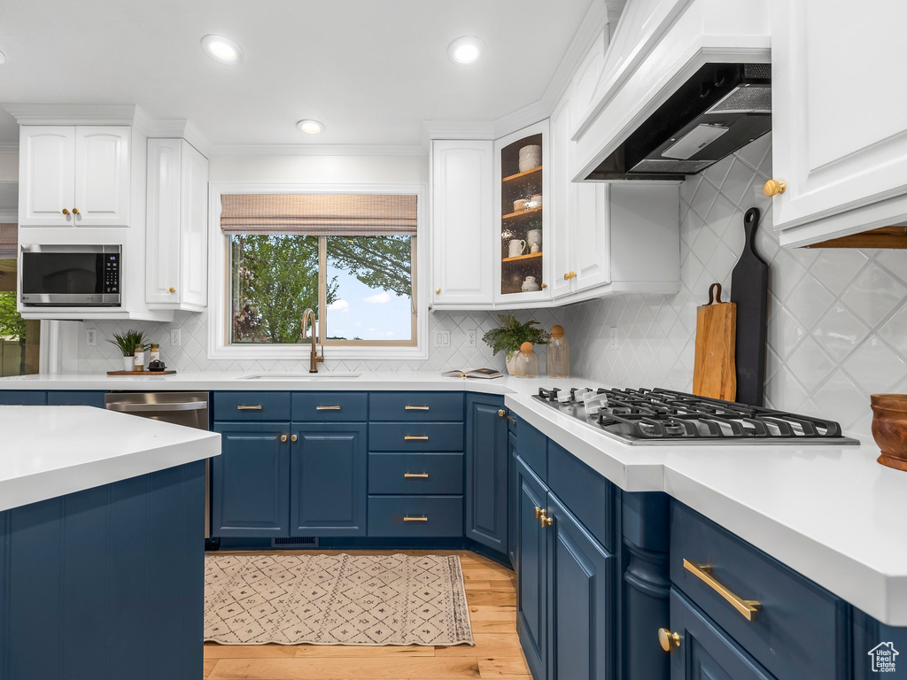 Kitchen with backsplash, appliances with stainless steel finishes, custom range hood, white cabinetry, and blue cabinets