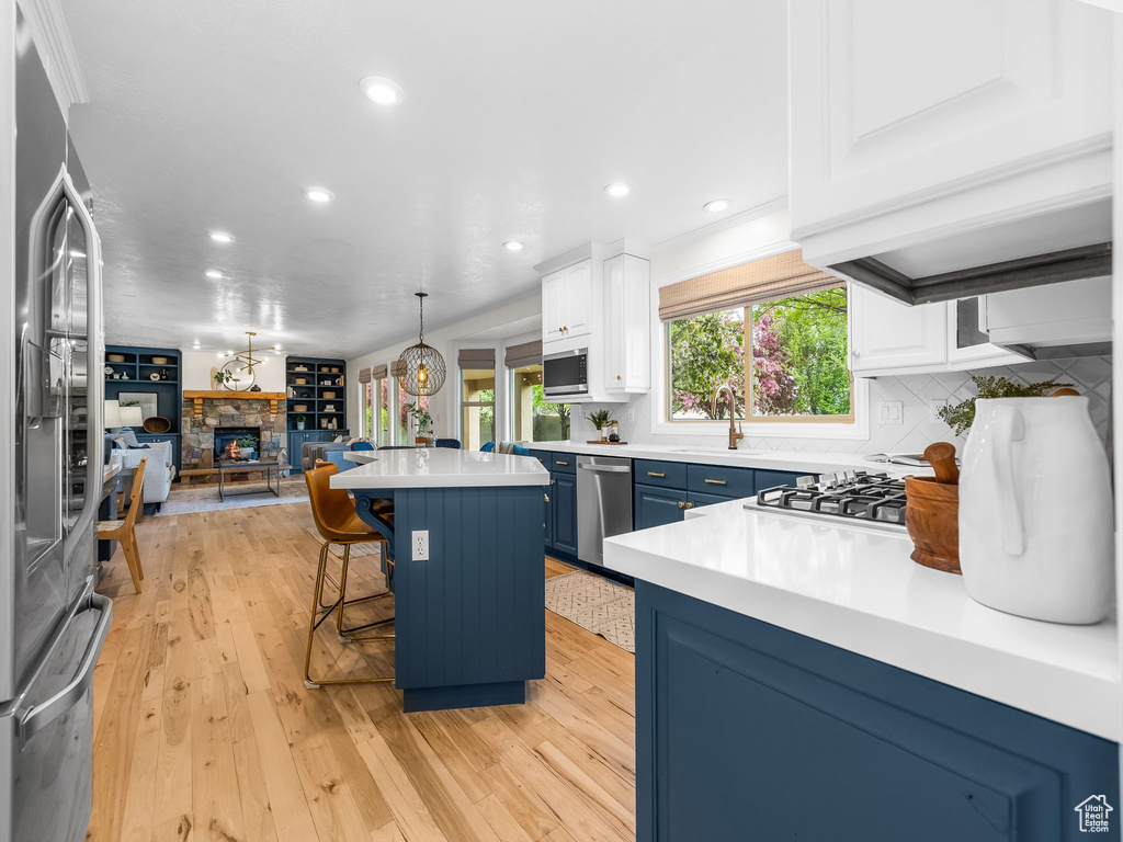 Kitchen with a stone fireplace, light hardwood / wood-style flooring, white cabinetry, a kitchen breakfast bar, and blue cabinets
