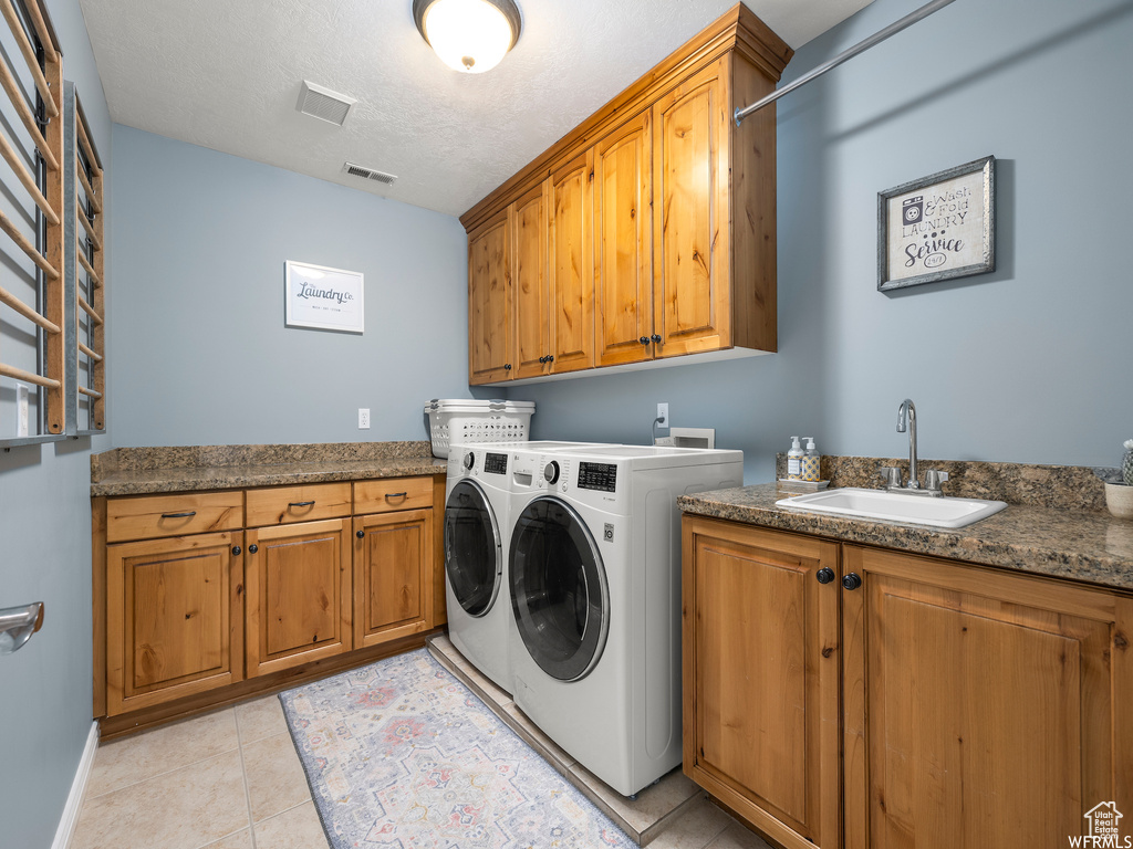 Laundry room with washing machine and clothes dryer, light tile floors, sink, cabinets, and a textured ceiling