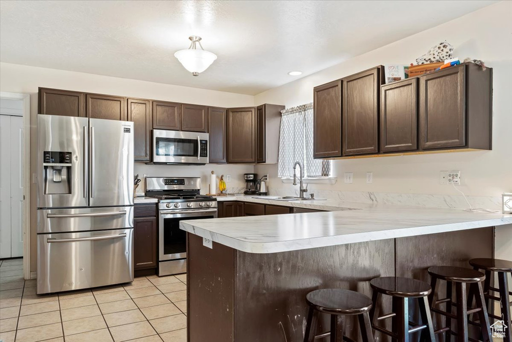 Kitchen with a kitchen breakfast bar, kitchen peninsula, appliances with stainless steel finishes, light tile floors, and sink