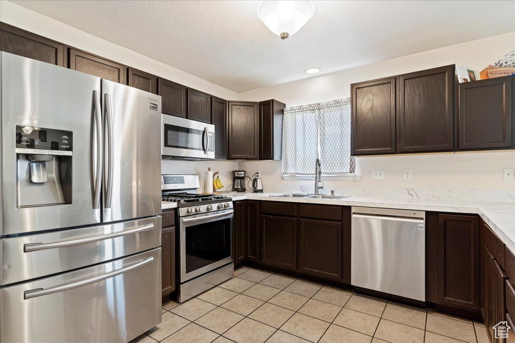 Kitchen featuring appliances with stainless steel finishes, light tile floors, sink, and dark brown cabinetry
