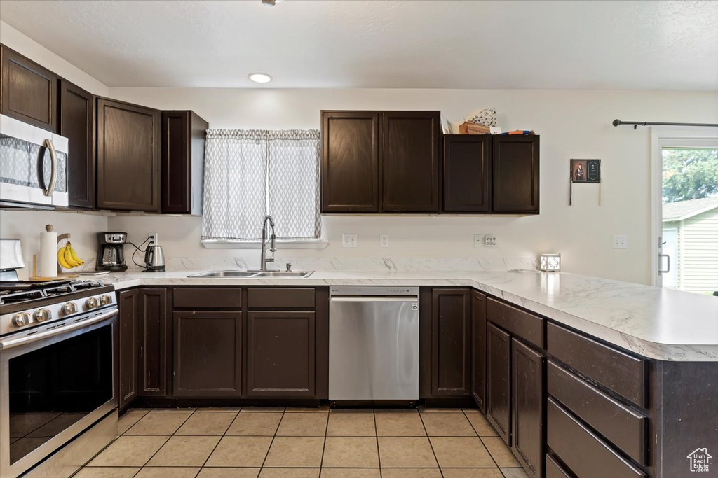 Kitchen featuring kitchen peninsula, stainless steel appliances, light tile floors, sink, and dark brown cabinetry