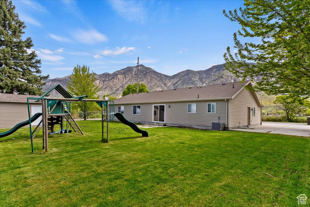 Rear view of house featuring a mountain view, a playground, central AC unit, and a lawn