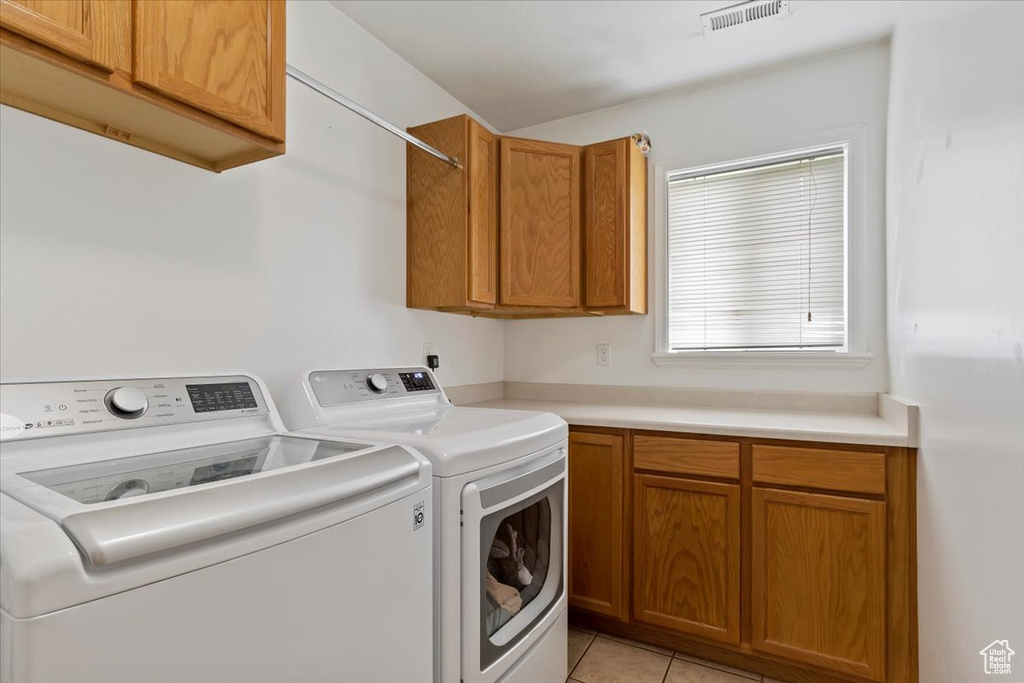 Laundry room with washing machine and dryer, light tile flooring, and cabinets