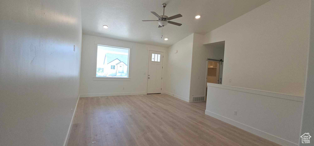 Empty room featuring a barn door, light hardwood / wood-style floors, ceiling fan, and lofted ceiling