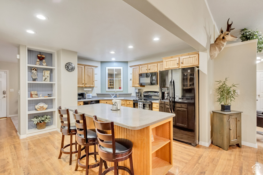 Kitchen with a center island, a breakfast bar, sink, black appliances, and light hardwood / wood-style flooring