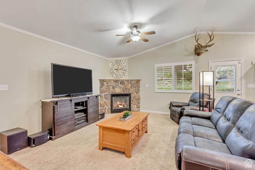 Carpeted living room featuring vaulted ceiling, ceiling fan, crown molding, and a stone fireplace