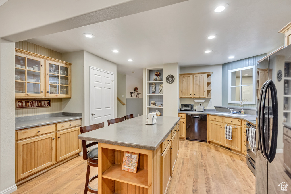 Kitchen featuring light brown cabinetry, light hardwood / wood-style flooring, a center island, and black appliances