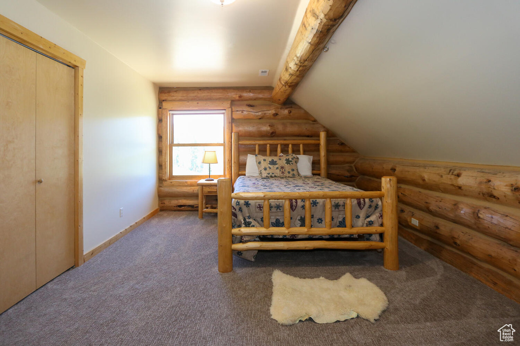 Carpeted bedroom featuring a closet, log walls, and vaulted ceiling with beams