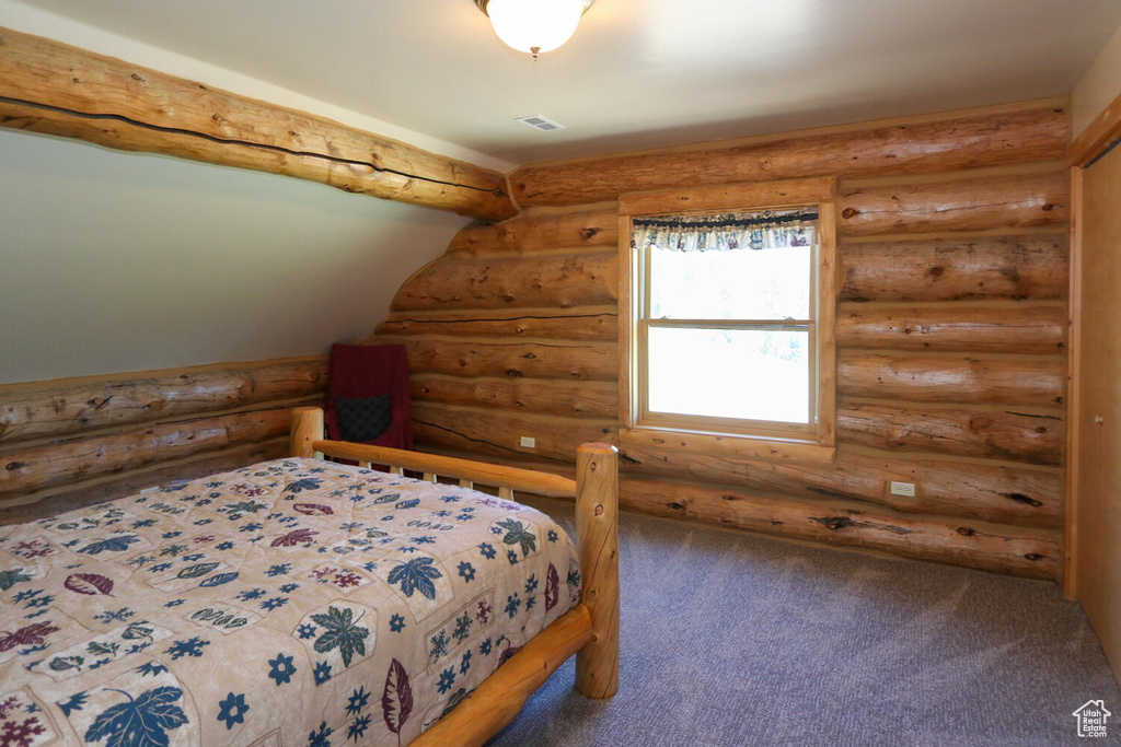 Bedroom with log walls and carpet flooring