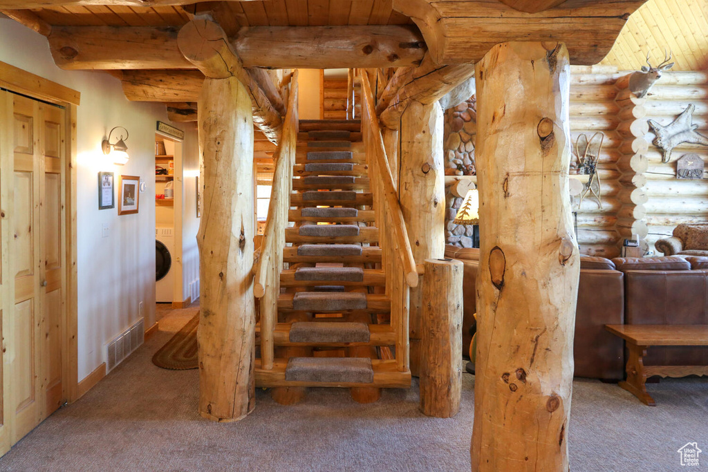 Staircase with wooden ceiling, log walls, and carpet flooring